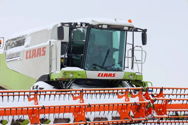Lviv, Ukrayna - 07 Ocak 2026: Bir Claas Lexion 'un güçlü taksisi ve parlak turuncu başlığı donmuş bir kış tarlasının ortasında taze karla kaplanmıştır..
