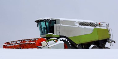 Modern hasat makineleri taze karla kaplıdır. Kireç yeşili vücut ile soğuk kış atmosferi arasında çarpıcı bir kontrast yaratır..