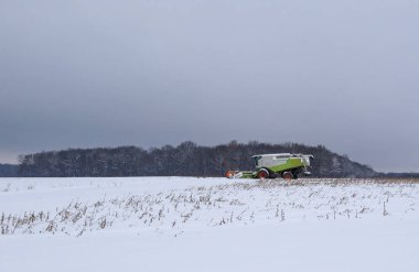 Bir biçerdöver, alçak bir Aralık semalarında geniş bir kar tarlasında hasat yapıyor..