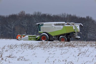Yoğun bir ormana karşı karlı bir tarlanın ortasında, çalışmayı ya da teknik bir mola vermeyi bekleyen bir biçerdöver duruyor..