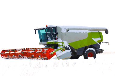 Parlak kırmızı başlıklı modern bir tahıl biçme makinesi gri bir kış gökyüzünün altında karla kaplı bir tarlanın ortasında duruyor..