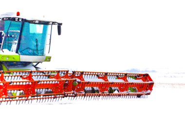 Büyük kırmızı başlıklı modern bir tahıl biçme makinesi kış tatilinde karla kaplı bir alanda duruyor. Güçlü tarım makineleri kısmen taze karla kaplıdır, belirgin bir kontrast yaratır ve