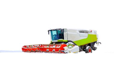 Güçlü bir modern biçerdöver ve parlak kırmızı bir başlık geniş beyaz karla kaplı bir tarlanın ortasında duruyor. Tarım makineleri tamamen karla çevrili parlak bir kış gökyüzünün altında,