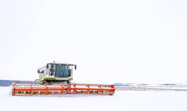 Güçlü bir tarımsal biçerdöver, kış boyunca geniş bir kar tarlasının ortasında durur..