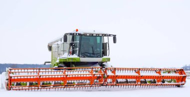 Parlak turuncu başlıklı bir biçerdöver kış ayazları sırasında karlı bir tarlanın ortasında durur. Tarım makinesi tamamen kar ve kar ile kaplı. Bu da şiddetli hava koşulları nedeniyle tarla çalışmalarının durdurulduğunu gösteriyor..