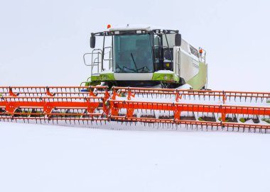 Modern bir hasat makinesinin büyük bir kabini ve turuncu başlığı beyaz karlı bir çölün ortasında yakın planda çekiliyor..