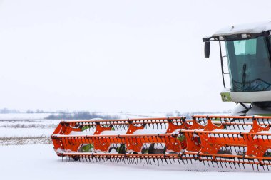 Parlak turuncu başlıklı modern bir zirai hasat aracı, saf beyaz kar zeminine karşı ayrıntılı bir şekilde yakalanır. Büyük hasat makineleri kış deposunda.,