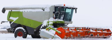 Geniş bir kar tarlasına karşı devasa turuncu başlıklı profesyonel bir tahıl biçicisinin detaylı bir görüntüsü..