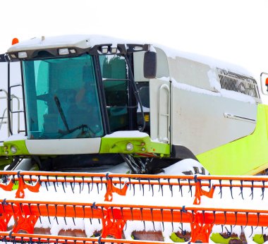 Modern bir hasat aracının yakın çekimi ve kış uykusunda taze kar tabakasıyla kaplı bir vücut. Güçlü tarım makineleri, minimalist beyaz arka planla parlak bir tezat oluşturuyor,