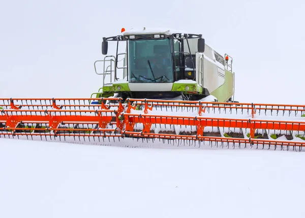 Modern bir hasat makinesinin büyük bir kabini ve turuncu başlığı beyaz karlı bir çölün ortasında yakın planda çekiliyor..