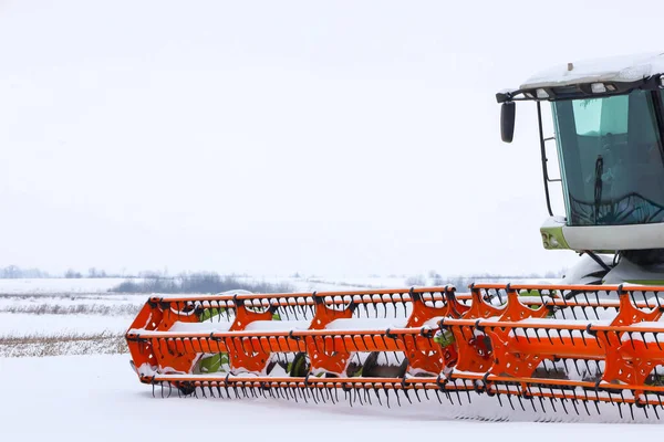 Parlak turuncu başlıklı modern bir zirai hasat aracı, saf beyaz kar zeminine karşı ayrıntılı bir şekilde yakalanır. Büyük hasat makineleri kış deposunda.,