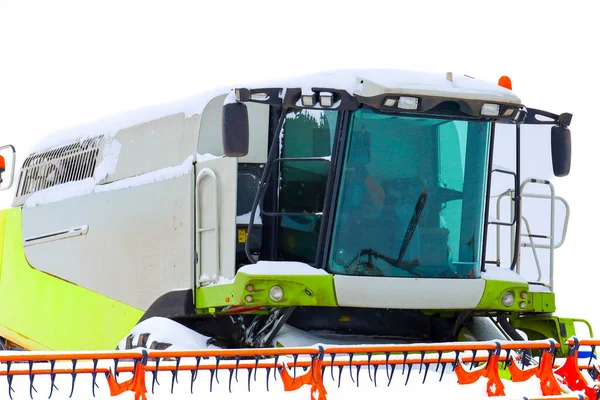 Kış mevsiminde taze kar tabakasıyla kaplı modern tarım makinelerinin yakın çekimi. Devasa kabin ve parlak yapısal elementler, minimalist beyaz arka planla tezat oluşturarak, teknolojik