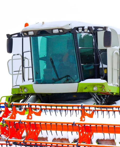 Kış mevsiminde kar ve don tabakasıyla kaplı modern bir tahıl hasadının üst kısmına dair detaylı bir bakış açısı. Taksinin devasa yapısı ve çalışan elementler minimalist beyaz gökyüzü ile çelişiyor.,