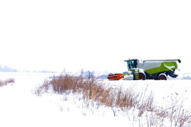 Kış uykusunda karlı bir tarlanın ortasında duran modern bir tarım biçicisinin geniş bir görüntüsü..