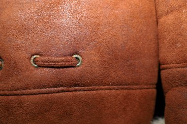 Yumuşak kahverengi süetin detaylı dokusu ya da karakteristik bir şekerleme ve dekoratif kordonlu metal bir göz merceği içeren koyun derisi bir ceket. Bu nesnenin düzgün bir yatay dikişi var. Kışın dış giyiminin dikim kalitesini ve doğal malzemesini gösteriyor..