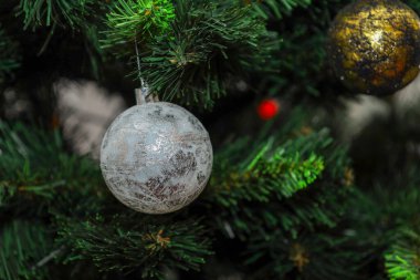 İki dekoratif top, siyah desenli gümüş ve altın, yapay bir Noel ağacının bereketli dallarını süslüyor..