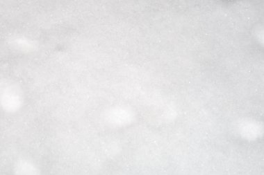 Yumuşak bir dokusu ve hafif don parıltılarıyla temiz bir kar yüzeyinin yakın çekimi. Üniformanın beyaz rengi ve ince düzensizlikler, kış mevsiminin saflığını, tazeliğini ve sükunetini sembolize eden ideal bir doğal arka plan oluşturuyor..