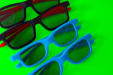 Dört çift parlak plastik 3D gözlük siyah ve mavi olarak zengin yeşil arka planda sıralanır. Modern film izleme aksesuarları dijital eğlenceyi sembolize eden şık bir geometrik kompozisyon oluşturur.,
