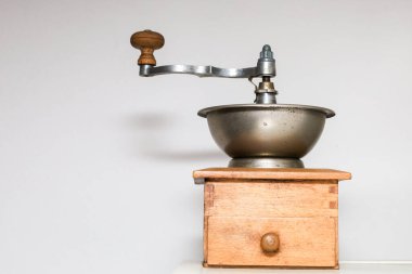 Ahşap gövdesi ve metal bir kâsesi olan klasik bir el yapımı kahve öğütücüsü, arka planda hafif bir arka planda duruyor..