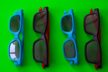 Dört çift mavi ve siyah-kırmızı çerçeveli gözlük parlak yeşil arka planda sıralanmıştır. Aksesuarların bu ritmik bileşimi, modern tasarım ve zengin renkleri tek bir kavramsal renkte birleştirerek farklı bir grafik etkisi yaratır.