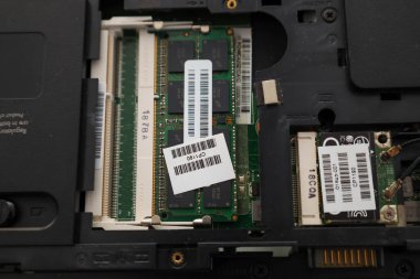 Yüklenmiş DDR RAM modüllerinin detaylı görüntüsü ve bir dizüstü bilgisayarın içindeki ağ kartı. Barkod etiketleri ve işaretleri donanım bileşenlerinin seri numaralarını ve teknik özelliklerini gösterir.