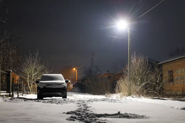 Yerleşim alanındaki sessiz, karlı bir cadde parlak bir sokak lambasıyla aydınlatılır. Uzun gölgeler ve taze kar üzerinde büyülü bir parıltı yaratır..