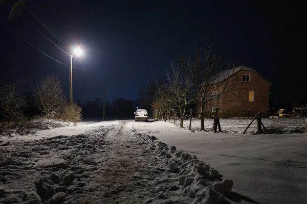 Karlı bir yolu aydınlatan parlak bir sokak lambası derin bir gece gökyüzünün altındaki ıssız bir eve götürüyor. Soğuk mavi akşam ile penceredeki sıcak ışık arasındaki zıtlık, karlı banliyölerde huzur ve huzur ortamı yaratıyor..