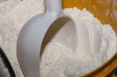 İnce beyaz buğday unu büyük bir kabı doldurur ve hafif kümelerle yumuşak bir doku yaratır. Plastik beyaz kepçe toza batırılır. Ekmek, hamur işi ya da profesyonel ev yemeği malzemelerini ölçmek için hazırdır..