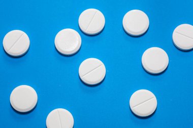 Beyaz yuvarlak haplar, parlak mavi bir arkaplana rastgele dağılmış. Farklı bir renk kontrastı yaratıyor..