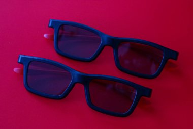 Kırmızı şakaklı bir çift klasik siyah 3D gözlük zengin bir kırmızı zemin üzerine yerleştirilir. Derin renk düzeni ve nesnelerin paralel düzeni modern bir sinemanın atmosferini mükemmel bir şekilde aktaran ve paylaşan şık bir kompozisyon oluşturur. .