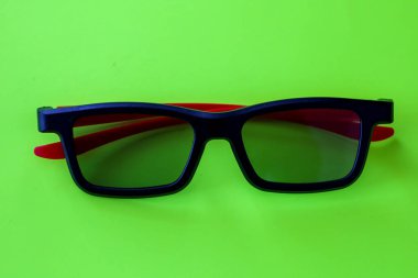 Parlak kırmızı tapınaklara sahip şık siyah 3D gözlükler zengin bir yeşil zemin üzerine kuruludur. Karşıt renk kombinasyonu modern sinema teknolojilerinin temasını mükemmel bir şekilde vurgulayan dinamik bir görsel efekt yaratır. .