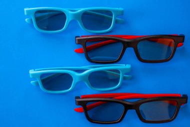 Cyan ve siyah-kırmızı çerçeveli dört çift modern 3D gözlük canlı bir mavi arka planda düzenlenmiştir. Stereoskopik filmleri izlemek için şık aksesuarlar minimalist tarzda dinamik bir kompozisyon oluşturur..