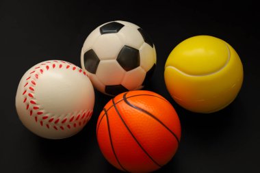 Dört popüler spor topu, futbol, basketbol, beyzbol ve tenisten oluşan bir koleksiyon, koyu siyah bir arkaplanda tek bir kompozisyonda toplandı..