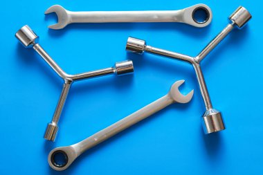 Çeşitli metal aletler, kombinasyon anahtarlar ve üçlü soket anahtarlar gibi, zengin mavi arka planda rastgele düzenlenmiştir..