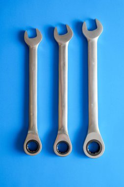 Parlak mavi arka planda paralel uzanan üç gümüş kombinasyon anahtarlar. Çeşitli boyutlarda profesyonel çelik aletler tamir, bakım ve çilingir işleri için tasarlanmıştır..