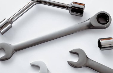 Temiz beyaz bir arkaplanda düzgünce yerleştirilmiş parlak çelik anahtarlar ve soketler koleksiyonu. Minimalist bileşim araçların metalik dokusunu ve profesyonel kalitesini vurgular,
