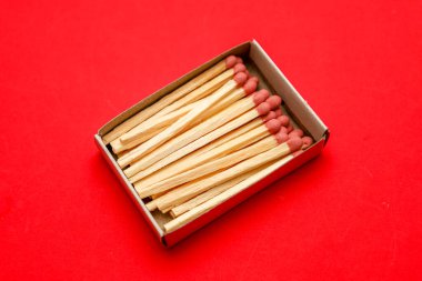 Kırmızı başlıklı yeni ahşap kibritlerle dolu açık bir karton kutu parlak kırmızı bir arka planda yatıyor. Bu monokrom ve minimalist kompozisyon potansiyel bir enerji hissi yaratır ve güvenlik kavramları için mükemmeldir.,