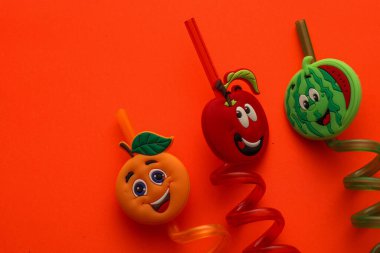 Lviv, Ukrayna - 25 Şubat 2026: Portakal, elma ve karpuz şeklinde komik karakterli neşeli ve parlak kıvrımlı pipetler zengin bir turuncu zemin üzerine kurulmuştur.