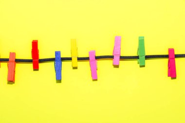 Siyah bir kabloya yerleştirilmiş çok renkli ahşap mandallar geniş bir kopya alanına sahip parlak sarı bir arka plana karşı. Bu minimalist kompozisyon ev idaresini, neşeli havayı ve günlük görevlere yaratıcı yaklaşımı sembolize eder..