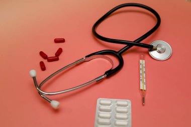 Şeftali arkaplanına karşı stetoskop, termometre ve çeşitli haplar içeren tıbbi bileşim. Durgun yaşam, hastalık tanısı ve tedaviye kapsamlı bir yaklaşım sergiliyor.,