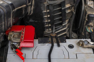 A car battery under the hood of a vehicle with red charging clamps connected during routine maintenance. This detailed shot of the engine compartment illustrates the battery charging process or electrical system diagnostics,