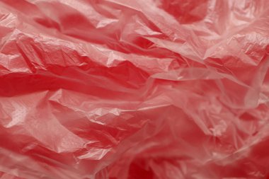 Bir makro çekim ince kırmızı bir plastik torbanın karmaşık soyut dokusunu ve sayısız kırışıklık ve kırışıklıkları gösterir. Detaylı polietilen yüzeyi aşırı derecede sentetik madde sorununu vurgulayan bir ışık ve gölge oyunu yaratıyor.