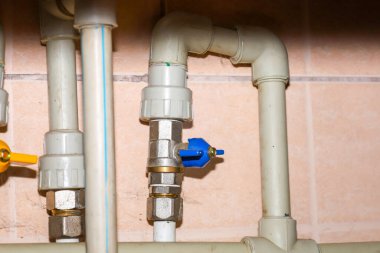 Plastik boruları olan su tedarik sistemi bileşenleri ve fayanslı duvara dayanan mavi saplı metal bir valf. Tesisat iletişiminin bu detaylı görüntüsü apartman yenileme için ideal.,