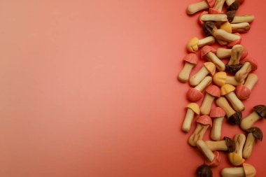 Renkli jöleli tatlı mantar şekilli kurabiyeler yoğun bir şekilde zengin pembe arka planda sağ kenar boyunca yerleştirilir. Sol taraftaki büyük boş alan, festival menüleri veya şekerleme reklamları için ideal bir kopya alanı sağlıyor..