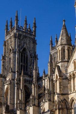A close-up shot of Gothic architecture featuring ornate stonework, spires, and arched windows against a clear blue sky in York, UK.