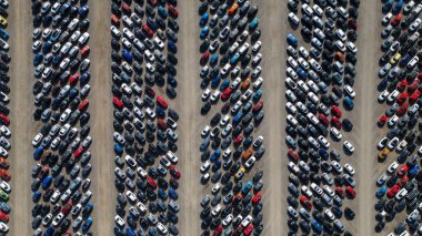 An aerial view captures a vast, organized parking lot filled with numerous cars of various colors, neatly arranged in rows on a dusty ground  at Copart yard, York, UK.
