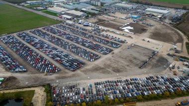 Aerial view of a large car storage facility with many rows of vehicles. Buildings, open land, and equipment are also visible  at Copart yard, York, UK.