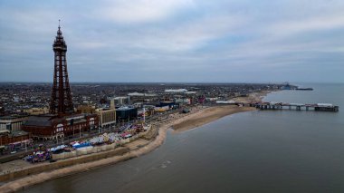 Önde gelen bir kulesi olan kıyı şehrinin havadan görünüşü, lunapark araçları, bir plaj ve Blackpool 'da bulutlu bir gökyüzünün altında denize uzanan bir iskele..