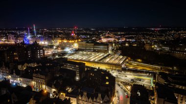 Aydınlatılmış binaları, camdan çatılı büyük bir tren istasyonu ve İskoçya 'nın Edinburgh şehrinde uzak bir dönme dolabı olan bir şehrin hava gece görüşü..