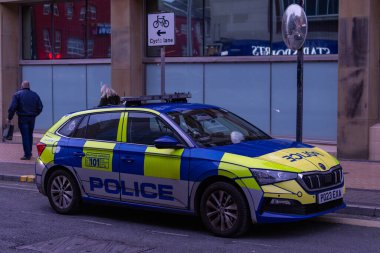 Mavi ve sarı bir polis arabası büyük pencereli bir binanın önündeki bir caddede park halinde..